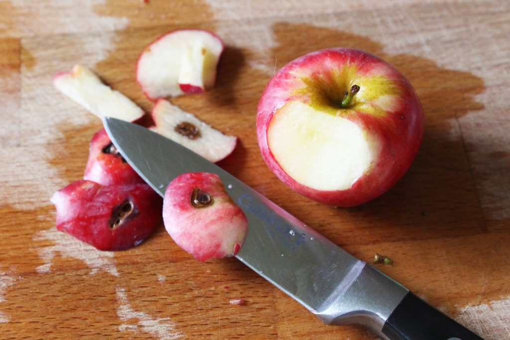 A photo of a blemish being cut off a red apple with a knife.